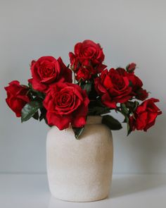 a white vase filled with red roses on top of a table