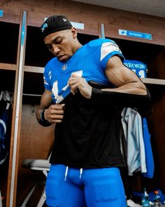 a man in a locker room holding onto his jersey and looking down at his pants