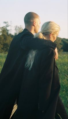 a man and woman are walking in the grass with their arms around each other as they hug