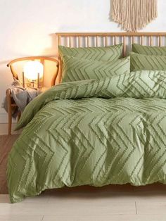 a bed with green comforter and pillows in a room next to a lamp on the floor