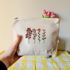 a hand is holding a small white bag with flowers on the front and bottom, along with a yellow checkered tablecloth