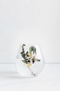 a glass vase with flowers in it sitting on a white countertop next to a wall