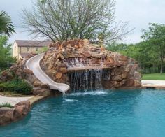 a pool with a slide in it next to a tree and water features on the side