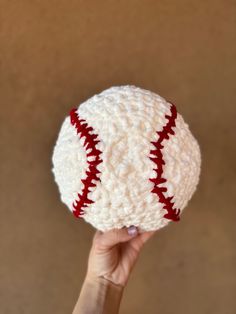 a hand holding up a crocheted baseball ball with red stitches on the outside