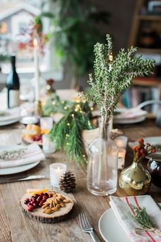 the table is set for christmas dinner with pine cones, berries and other holiday decorations