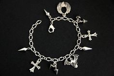 A collection of silver plated punk rock themed charms have been dispersed around a shimmering silver plated bracelet chain in this handmade charm bracelet. This rock n roll charm bracelet is then completed with a lobster clasp and a 1/2 inch of chain at the end for adjustable sizing. Charms in this bracelet include a winged skull charm, winged heart charm, two cross charms, three long spike charms, and four short spike charms. ● Sizing ● To determine your bracelet size, do a snug measurement of Rocker Metal Bracelets For Concerts, Silver Rocker Bracelets For Concerts, Handmade Metal Jewelry For Concert, Metal Rock Style Bracelets For Concerts, Alternative Metal Bracelet For Alternative Fashion, Adjustable Silver Grunge Bracelet, Emo Style Metal Dangle Jewelry, Emo Dangle Metal Jewelry, Grunge Metal Bracelets For Concerts