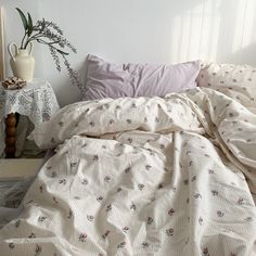 an unmade bed with white sheets and pink flowers on the comforter, next to a plant