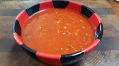 a red and black bowl filled with soup on top of a wooden table