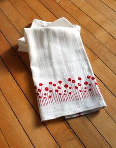 two white napkins with red flowers on them sitting on a wooden floor next to each other