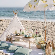 a picnic table set up on the beach with an umbrella over it and some food