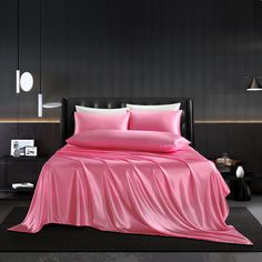 a bed with pink sheets and pillows in a black walled room, next to a night stand