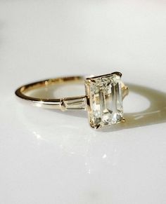 an engagement ring with a green diamond and two baguettes on the side, sitting on a white surface