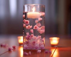 a glass vase filled with water and floating pink flowers on top of a wooden table