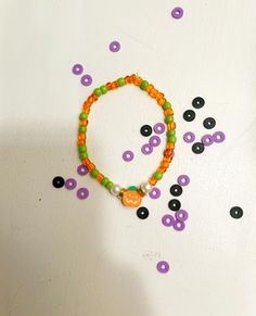 an orange and green beaded bracelet with black dots on it, surrounded by purple and green beads