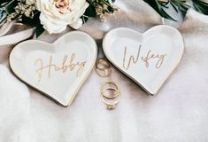 two heart shaped dishes with wedding rings and flowers on the table next to each other