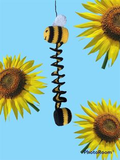 three sunflowers and one bee hanging from a string on a blue sky background