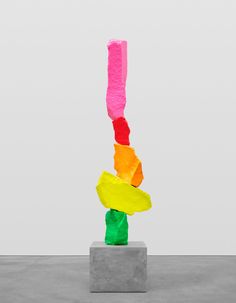 a sculpture made out of colored paper on top of a cement block in front of a white wall