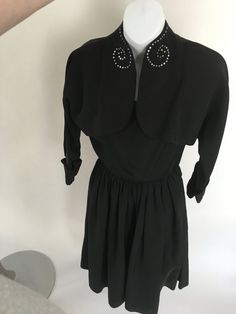 1950's/60's heavy black dress with bolero jacket with rhinestone swirls at the collar. In mint conditionSize XS: 23" waist and 33" bustMeasurements:DressB: 33" W:23"H: freeShoulder to waist: 16"Waist to hem: 26.5" Jacket/ BoleroBust from edge to edge: 40" Hem from edge to edge: 38"Sleeve length: 21.5Sleeve circumference: 16.5" around Retro Black Vintage Dress For Evening, 1950s Style Black Dress For Vintage Events, 1950s Style Black Vintage Dress, Black Adjustable Vintage Costume Accessories, Black 1950s Style Vintage Evening Dress, 1950s Style Formal Dress With Button Closure, 1950s Black Vintage Dress, 1950s Black Vintage Evening Dress, Black Vintage Outerwear With Double Button Closure