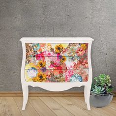 an old dresser with flowers painted on it and a potted plant next to it