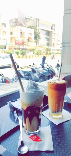 two drinks sitting on top of a table with spoons and napkins in front of them