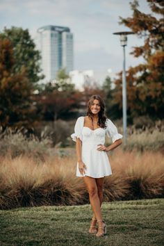 a beautiful woman in a white dress posing for a photo with her hands on her hips