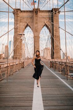 a woman in black dress walking across the brooklyn bridge with american flag on her head