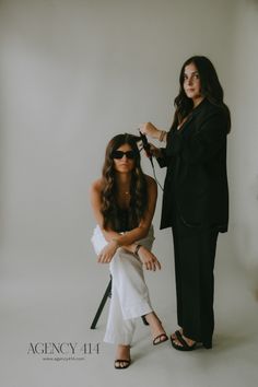 two women are sitting on a chair and one is getting her hair done