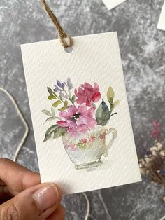 a hand holding up a card with flowers in the teacup on it and string