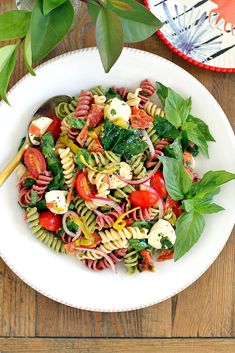 a white bowl filled with pasta salad on top of a wooden table next to a potted plant