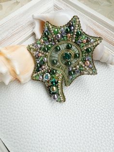 a green brooch sitting on top of a white piece of cloth next to seashells