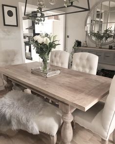 a dining room table with white chairs and flowers in a vase on the top of it