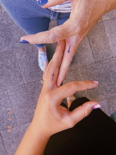 two people holding hands with cross tattoos on their fingers and the other hand pointing at each other