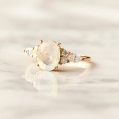 Capturing three popular stone cuts into one ring? Not a problem. Our Lauryn ring with oval Moonstone as the main stone, a pair of two round moissanite stones on the sides, and a marquise one to pull it all together into a cohesive and beautiful one-of-a-kind ring. Details: Center stone Gemstone: Moonstone Stone Shape: Oval Measurements: approx. 9x7mm Side stones Gemstone: Moissanite Shape: Round, Marquise Measurements: 2mm (4), 5x2.5mm (2) Band measurements: approx. 1.8mm wide, approx. 1.5mm thi Planet Ring, Moss Agate Ring, Moonstone Stone, Rose Quartz Ring, Round Moissanite, Agate Ring, Swiss Blue Topaz, Quartz Ring, One Ring