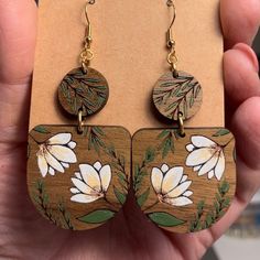 a pair of wooden earrings with white flowers painted on the front and back of them