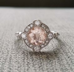 a fancy ring with a pink diamond surrounded by white diamonds on a gray surface in front of a black background