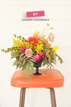 an orange stool with flowers on it in front of a white wall and a pink sign