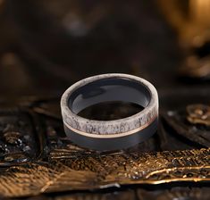 a wedding ring sitting on top of a gold and black surface with leaves around it