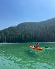 a person on a kayak in the middle of a lake with trees behind them