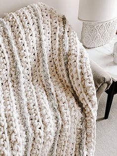 a white crocheted blanket sitting on top of a bed next to a lamp