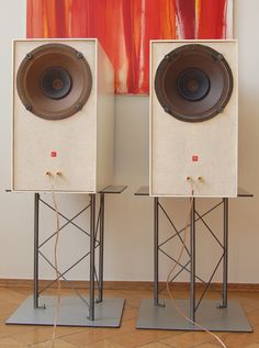 two speakers sitting on stands in front of a painting