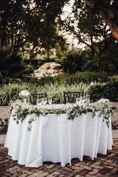 the table is set with white linens and greenery for an elegant wedding reception