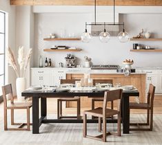 a dining room table and chairs in front of an open kitchen area with shelves on the wall