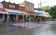 an empty street with shops and stores in the background on a rainy day, there is a large checkerboard dance floor