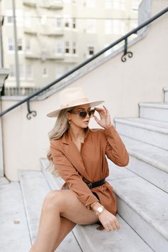 a woman sitting on the steps wearing a tan dress and hat with her legs crossed