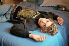 a young boy laying on top of a bed next to a blue comforter and pillows