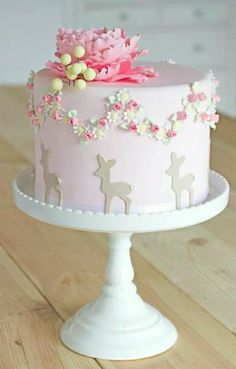 a pink and white cake with flowers on top is sitting on a wooden table in front of a window