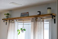 some plants are hanging on the window sill in front of two windows with white curtains