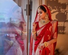 a woman in a red and white sari is standing near a window with her hands on her hips