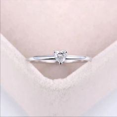 a heart shaped diamond ring sitting on top of a white blanket