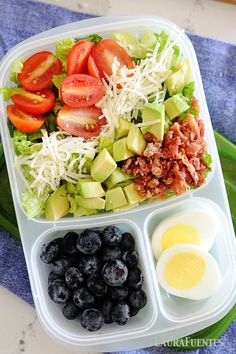 a plastic container filled with blueberries, avocado, tomatoes and other food